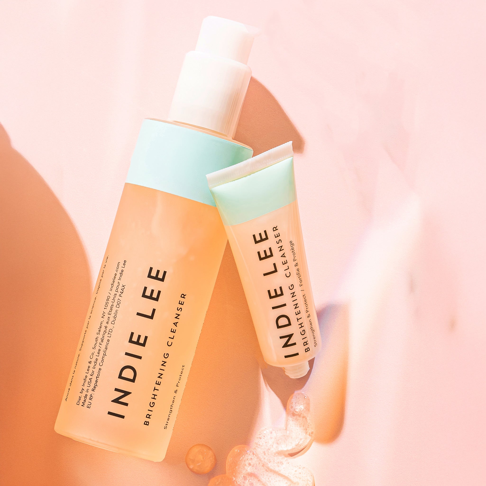Two bottles of Indie Lee Brightening Cleanser on a soft pink background