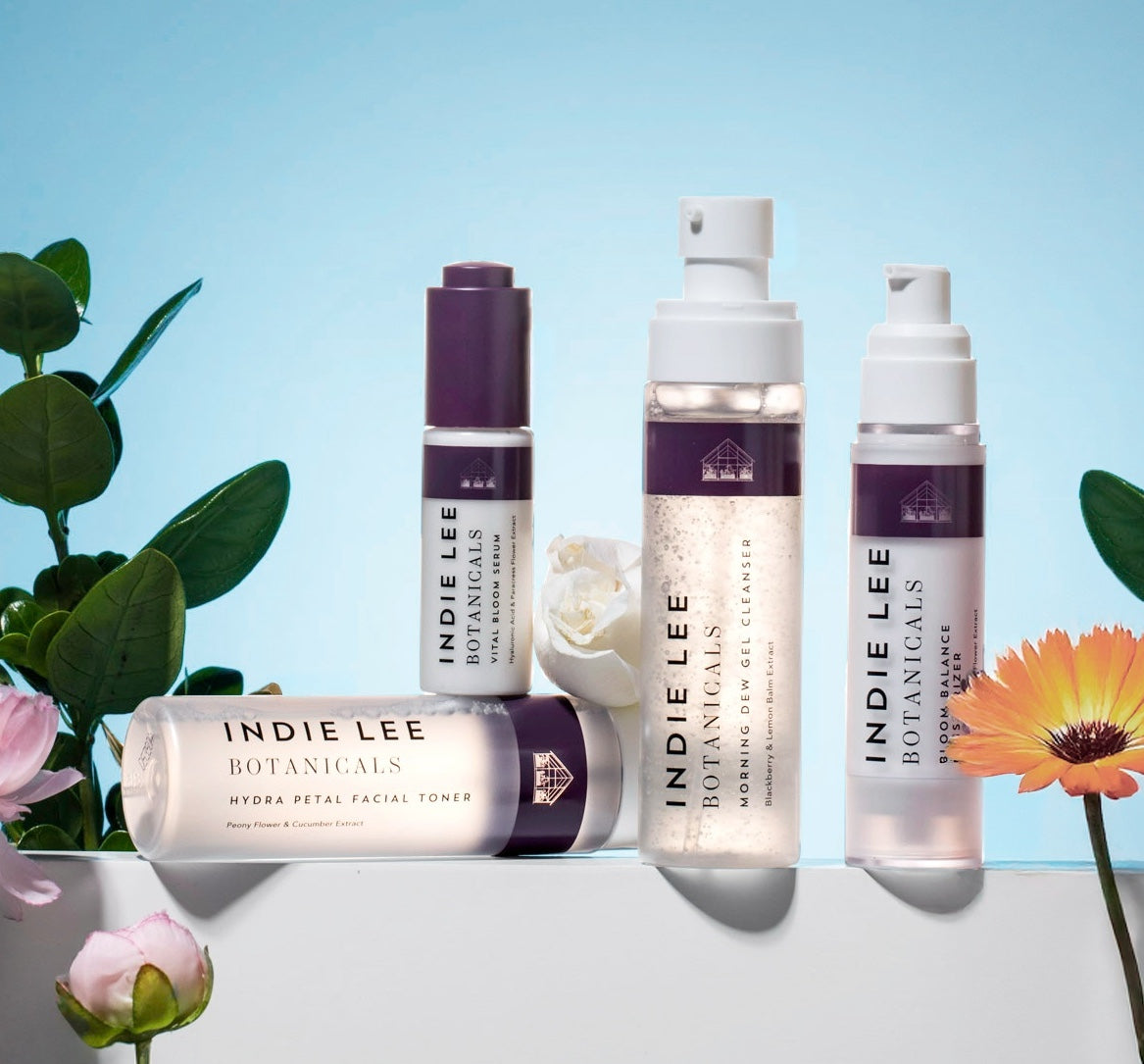 Indie Lee Botanicals skincare products with flowers on a light blue background