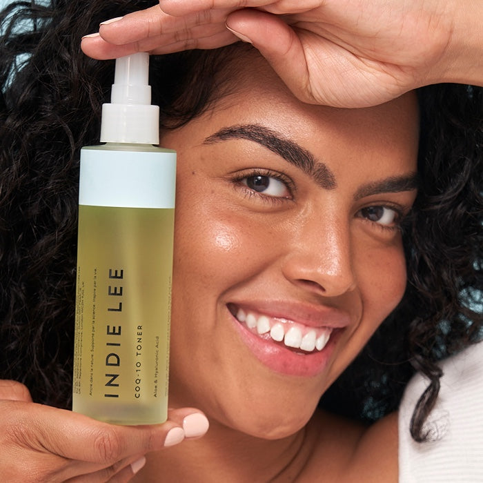 Woman holding a bottle of Indie Lee CoQ-10 Toner with a close-up on her face.