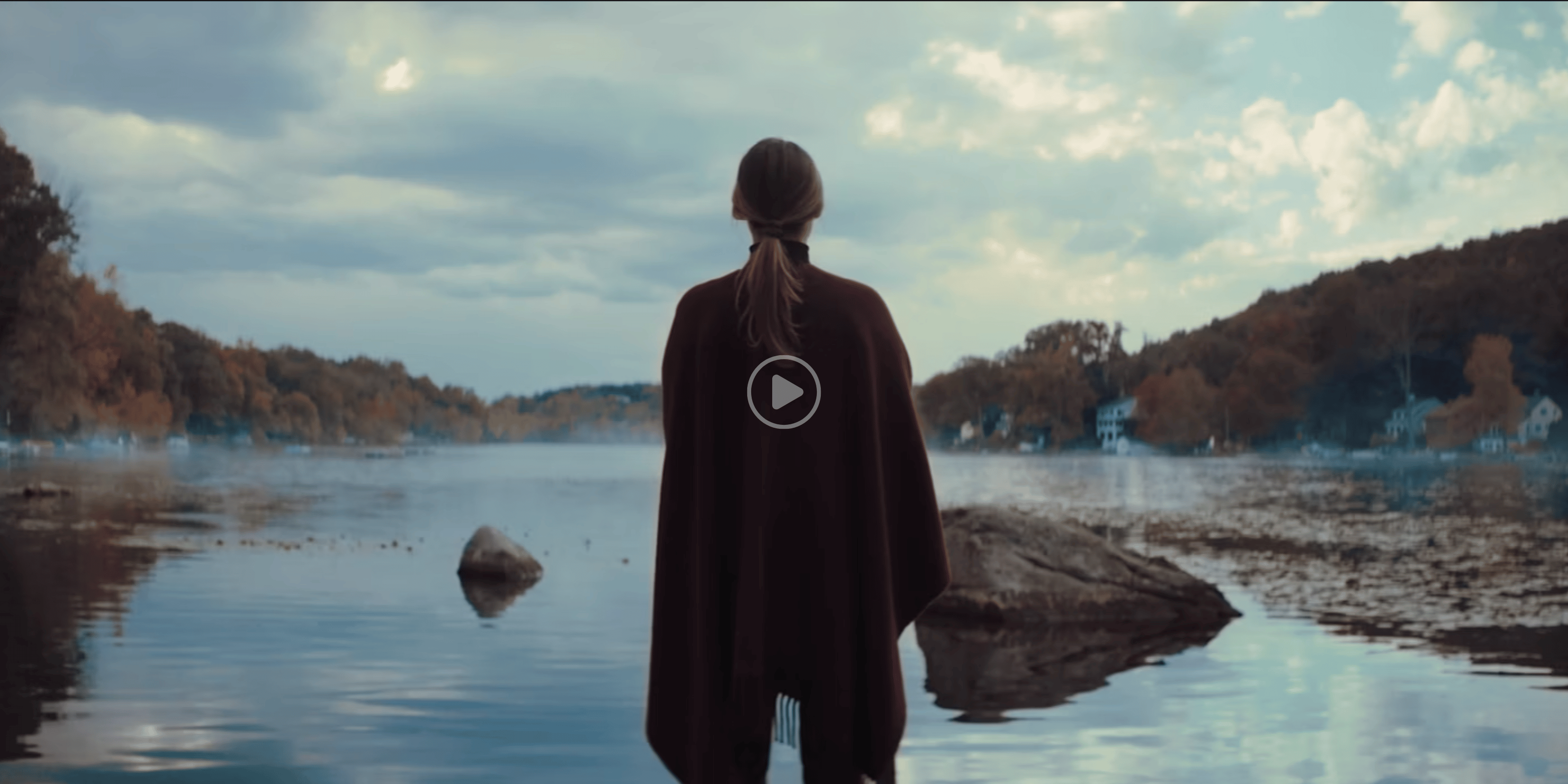 Indie Lee standing by a lake with a cloudy sky