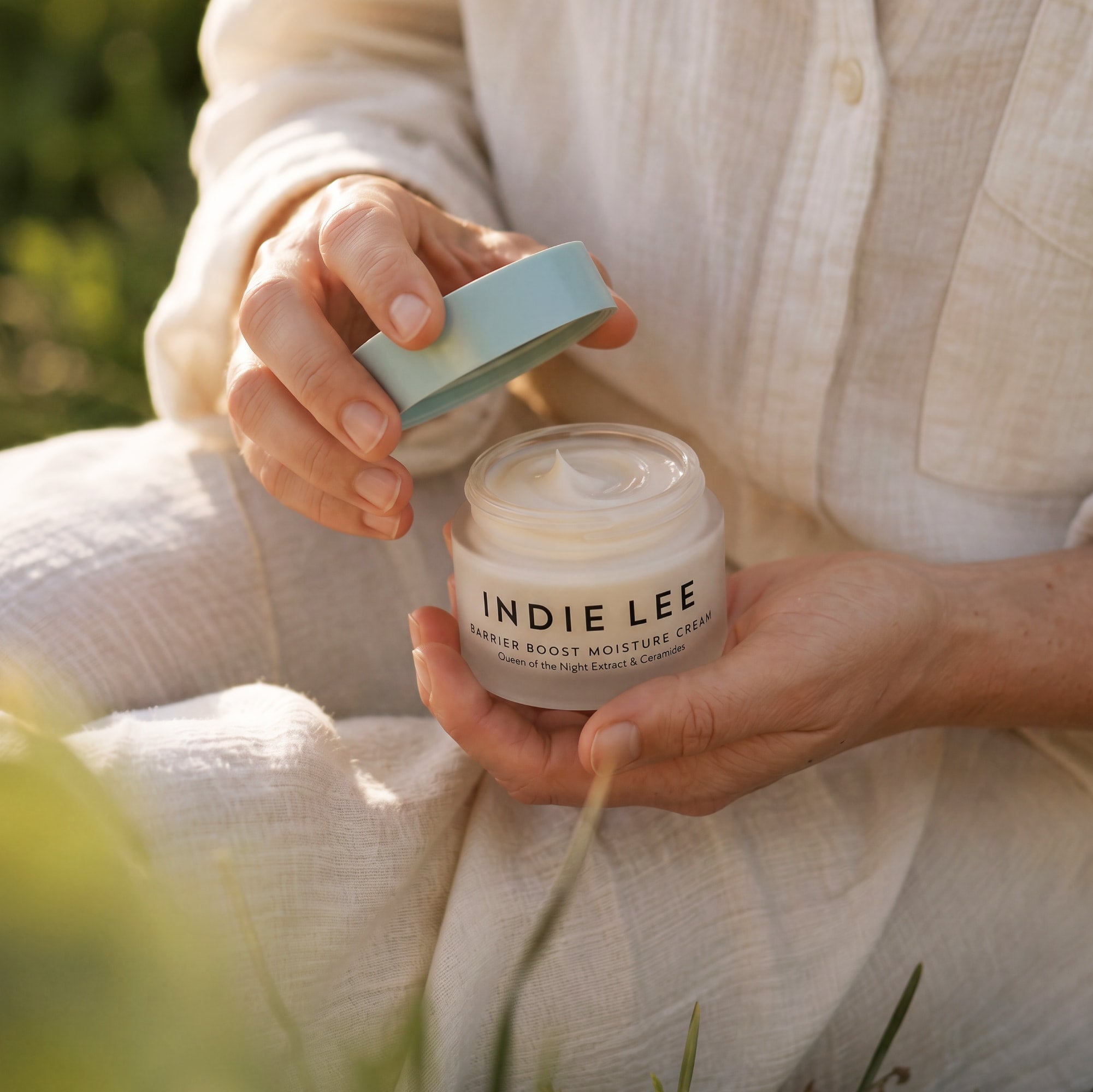 Woman holding an open jar of Indie Lee Barrier Boost Moisture Cream on a natural background