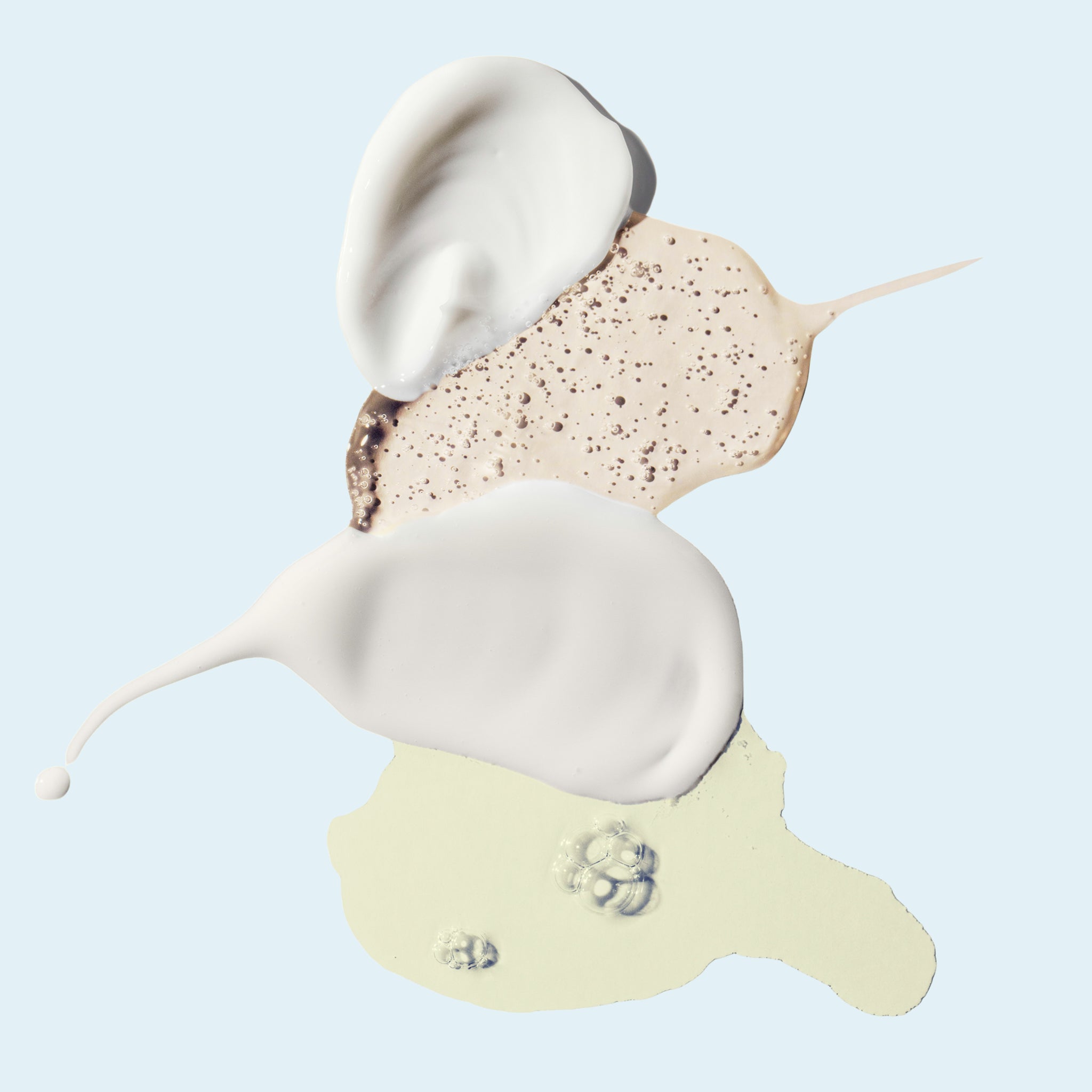 Three liquid product swatches with a cream-colored top, a speckled beige middle layer, and a pale yellow bottom layer on a light blue background.