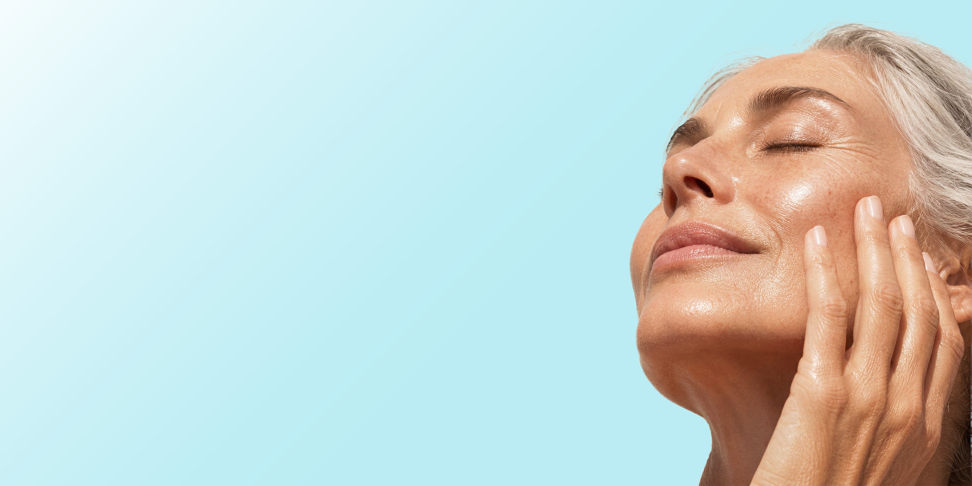 Close-up of a woman with closed eyes and her hand on her cheek, set against a solid light blue background.