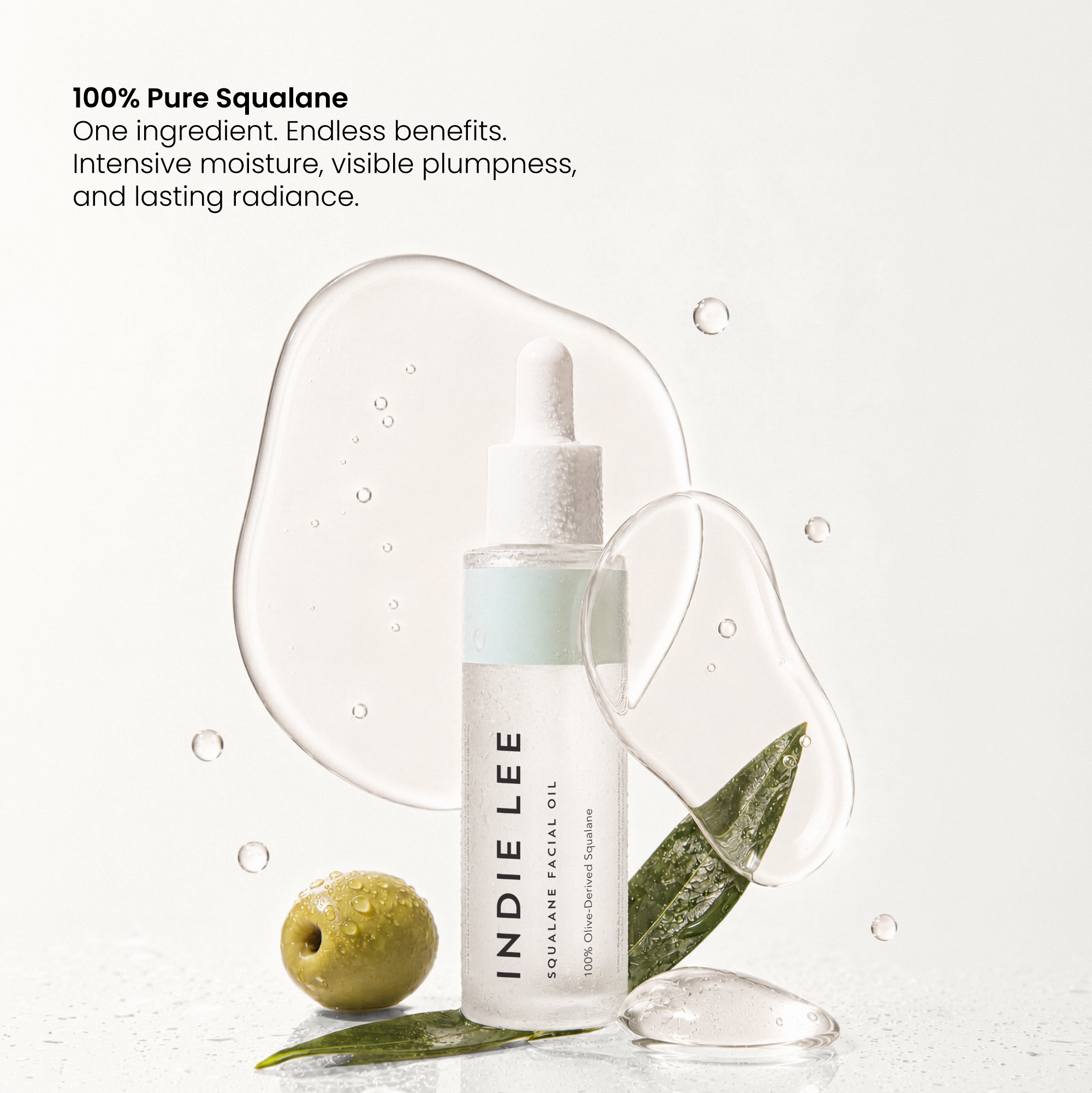 Indie Lee Squalane Facial Oil bottle styled with a green olive, leaves, and clear liquid droplets on a white background with text highlighting benefits.