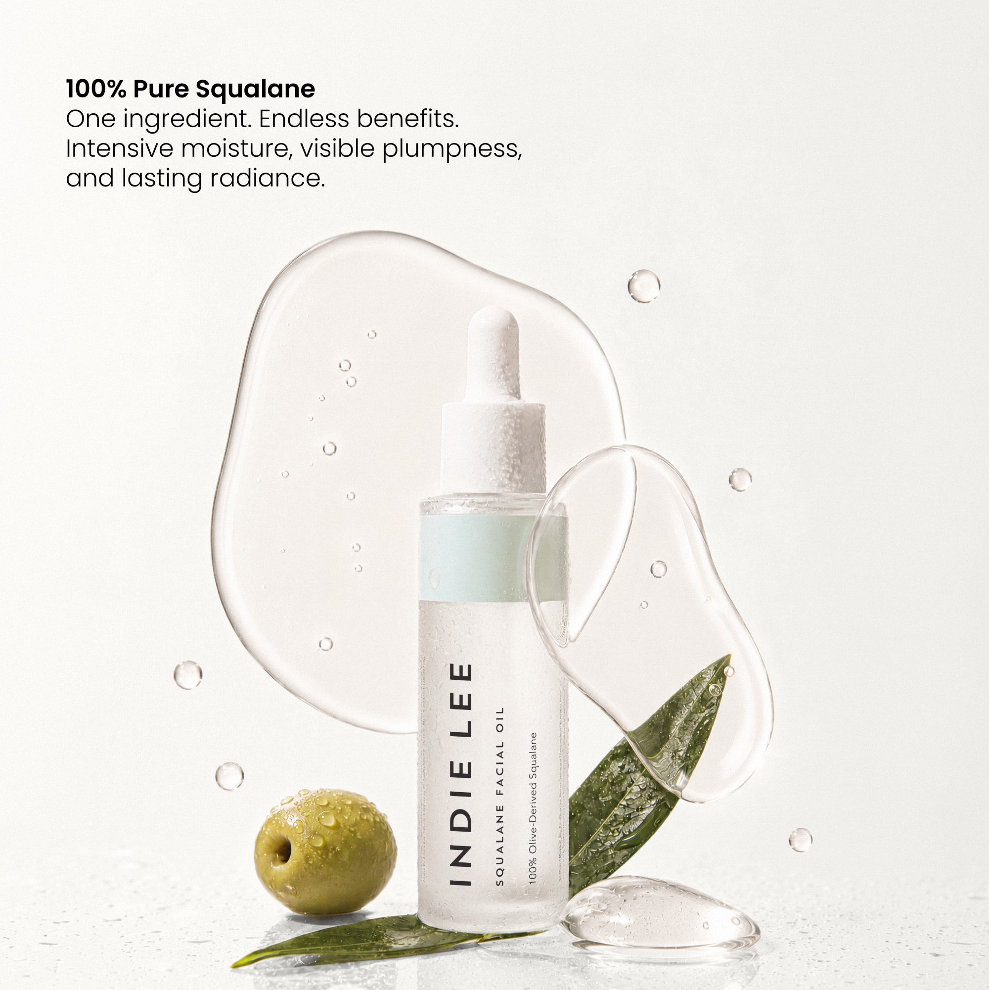 Indie Lee Squalane Facial Oil bottle with dropper, styled with a green olive, leaves, and clear liquid droplets on a white background with text highlighting pure squalane benefits.