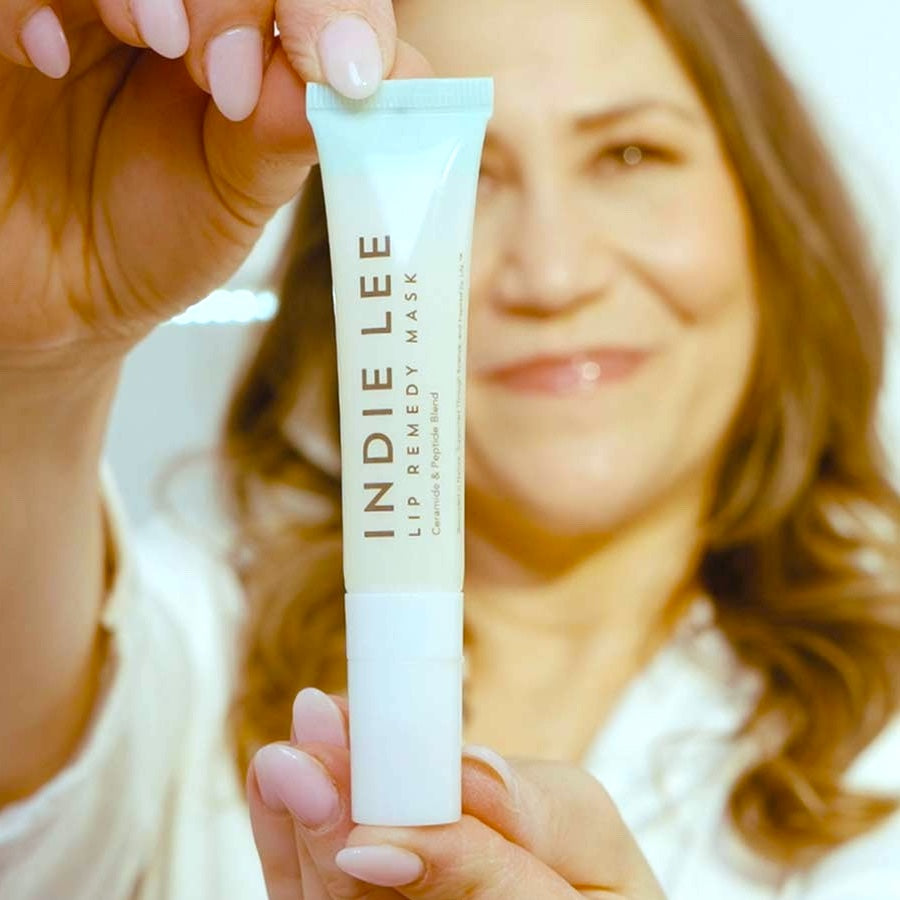 Indie Lee holding a tube of Lip Remedy Mask with a blurred background