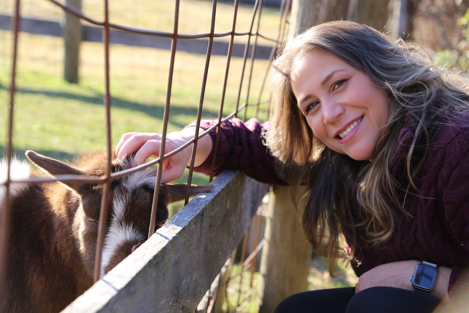 Indie Lee petting a goat through a fence in an outdoor setting
